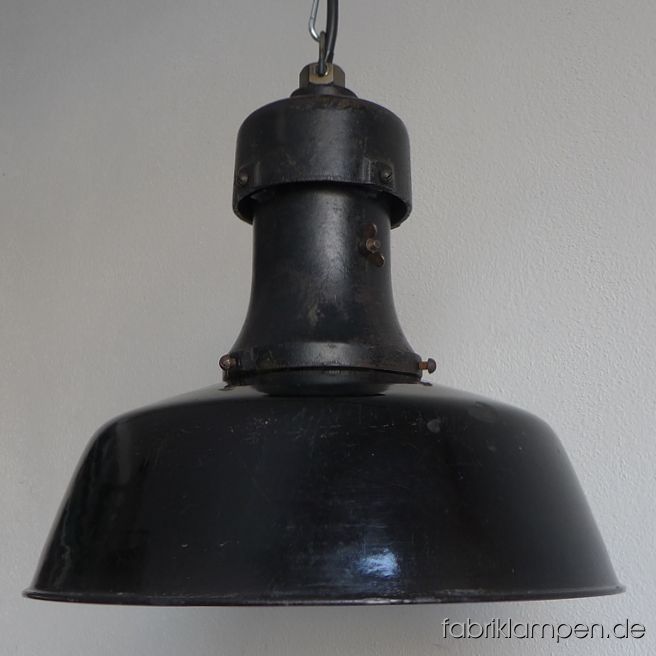 Antique black factory lamp with enamel shade and casted iron top. Very old, from the 1920ies. Material: black (inside white) enameled steel sheet, casted iron head. With very strong traces of age and usage. Cleaned, newly electrified, with E27 ceramic socket. Height of the lamp ca. 37 cm (14,6 inches), diameter of the shades ca. 40 cm (15,7 inches). The lamp will be shipped with 2 m cable and hanging eye. Chain suspension is possible for an additional charge. 